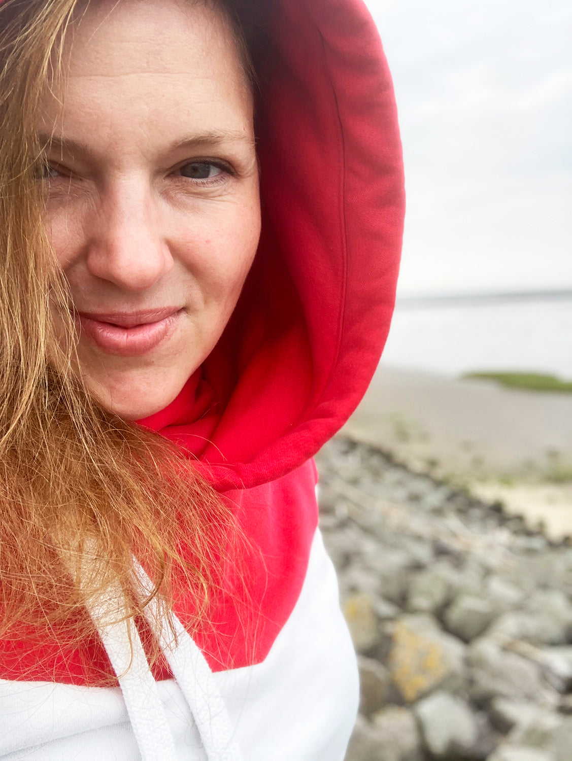 Portraitaufnahme von Christiane Kalkhake. Sie trägt einen rot-weißen Hoodie und ist am Meer.